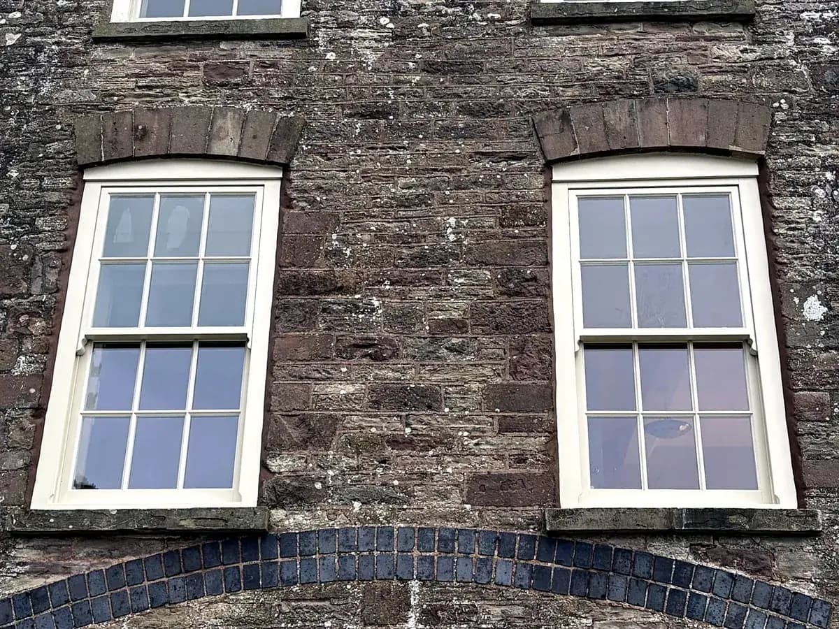 Two cream timber sash windows with curved heads in a Monmouthshire stone elevation