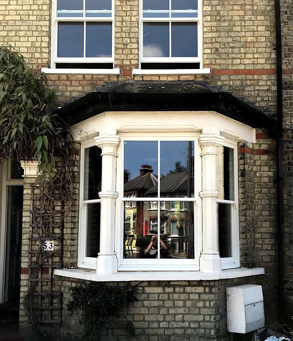 White timber Victorian bay sash window with turned mullion columns in yellow stock brick