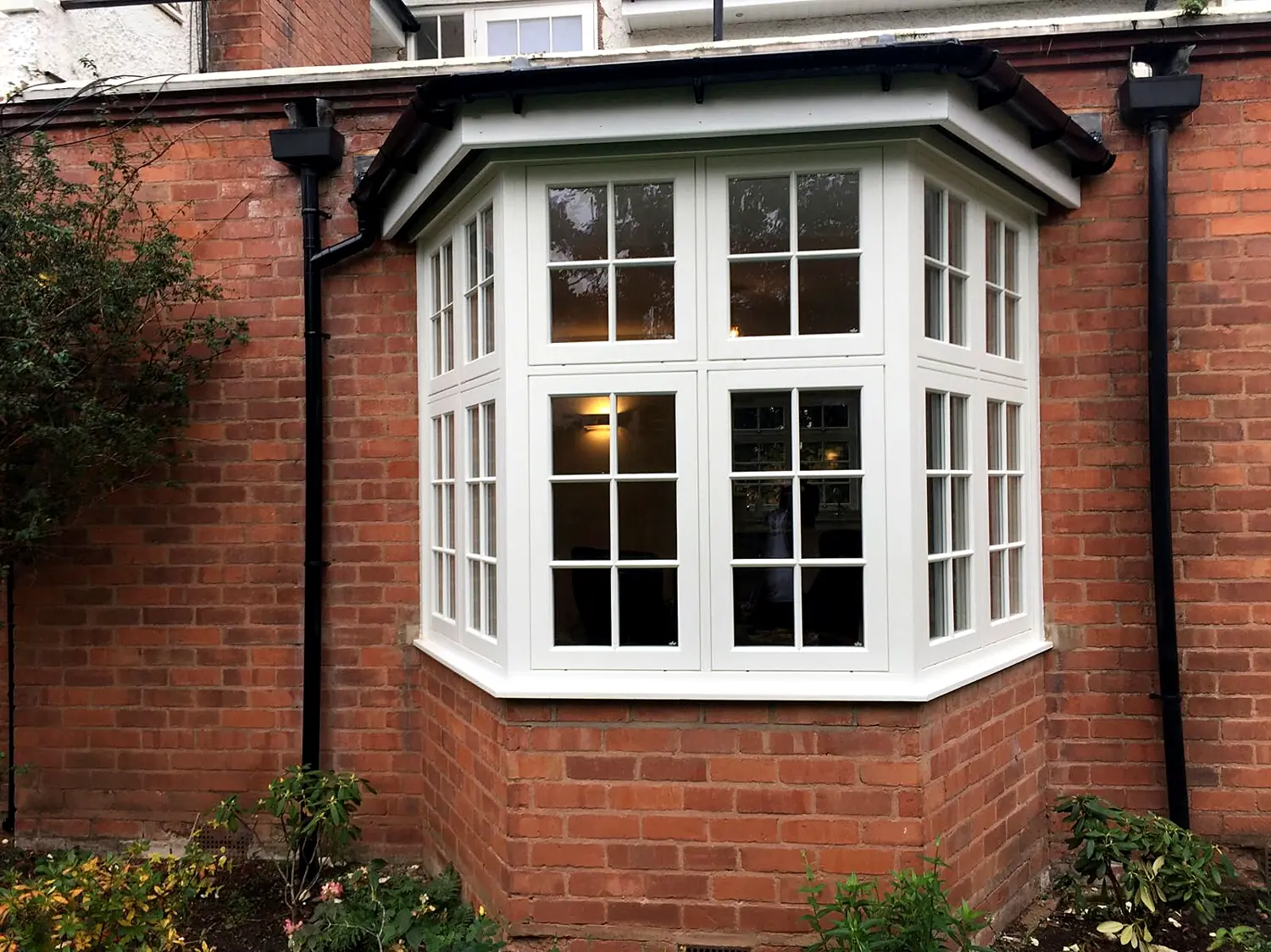 Cream timber splayed casement bay window with tiled roof in a red-brick house