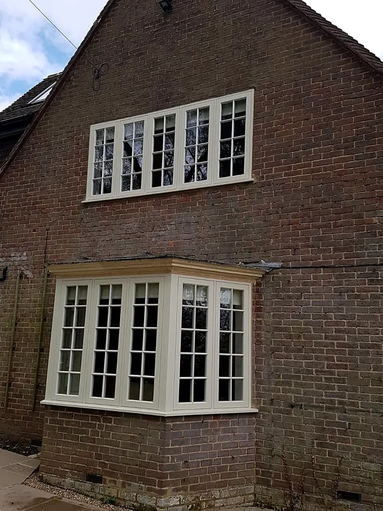 Cream timber splayed bay casement window with multi-pane glazing in a red-brick house