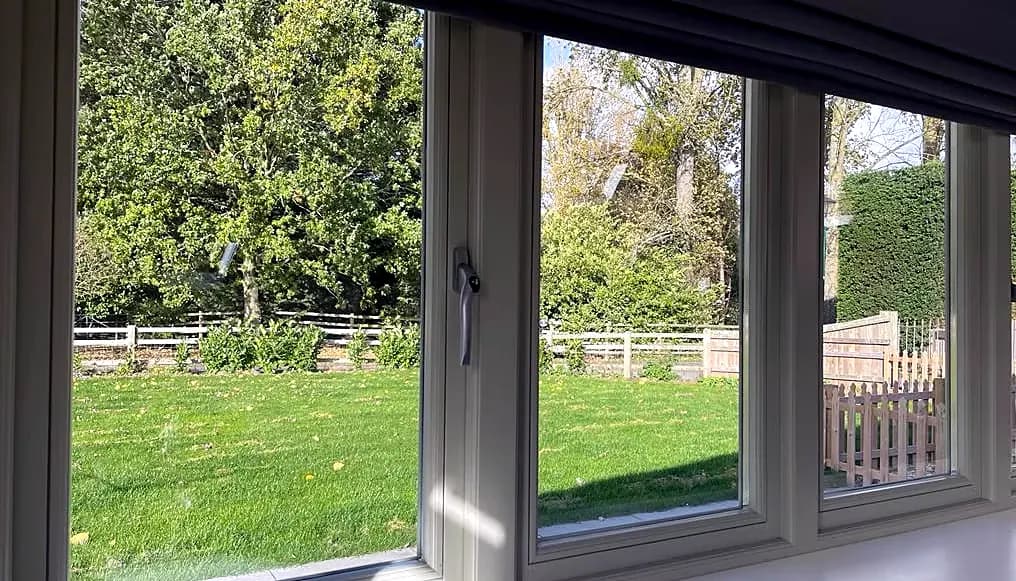 Interior view through cream timber flush casement windows onto a garden