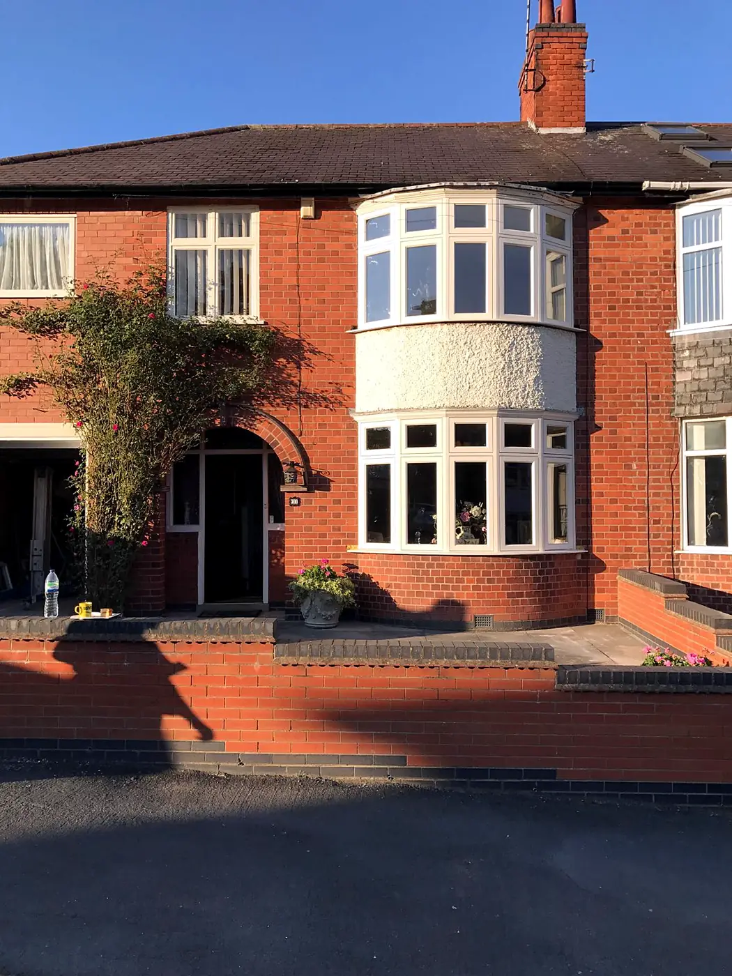 Red-brick semi-detached house with a two-storey cream timber bow casement bay in evening light