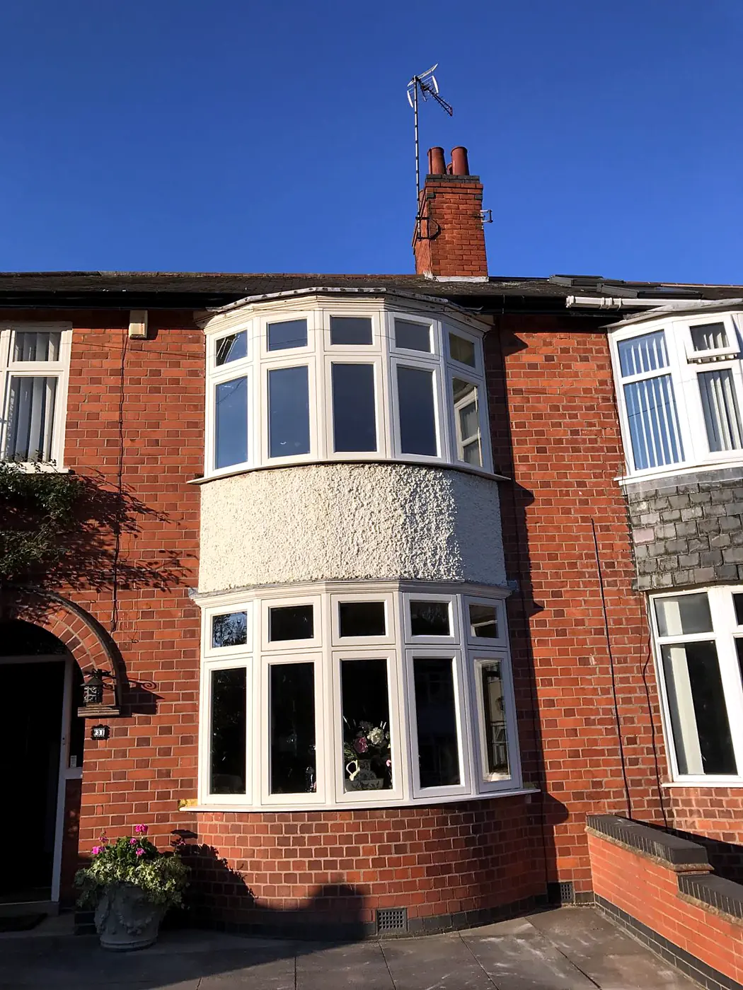 Cream timber curved bow casement bay window over two storeys on a 1930s red-brick house