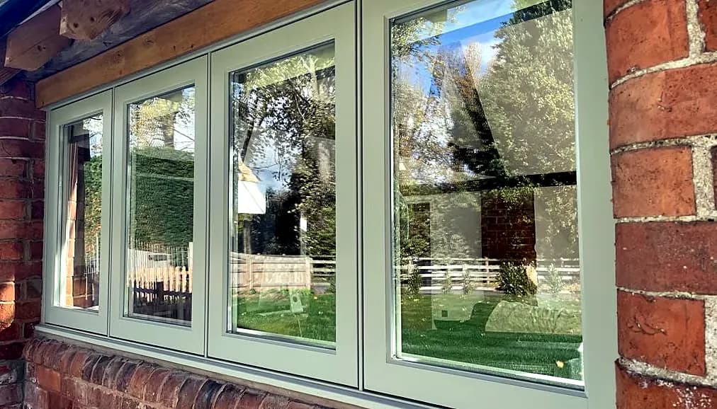 A run of sage-green timber flush casement windows in red brick with a timber lintel