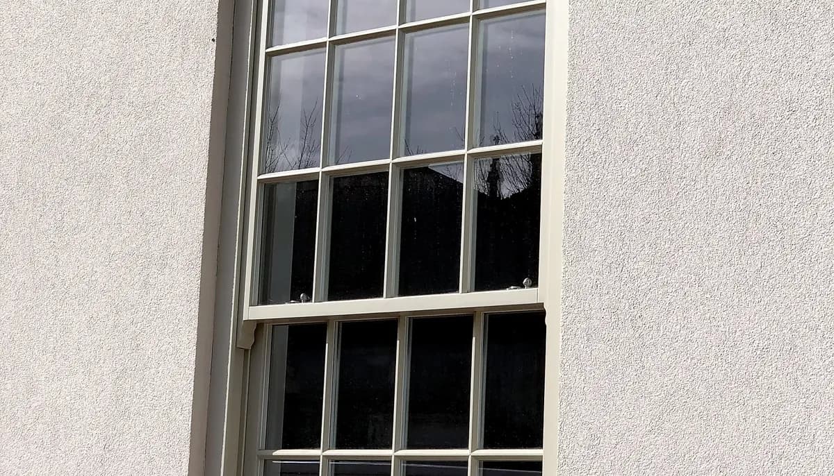 Detail of a cream timber Georgian sash window with slim glazing bars and brass sash fasteners