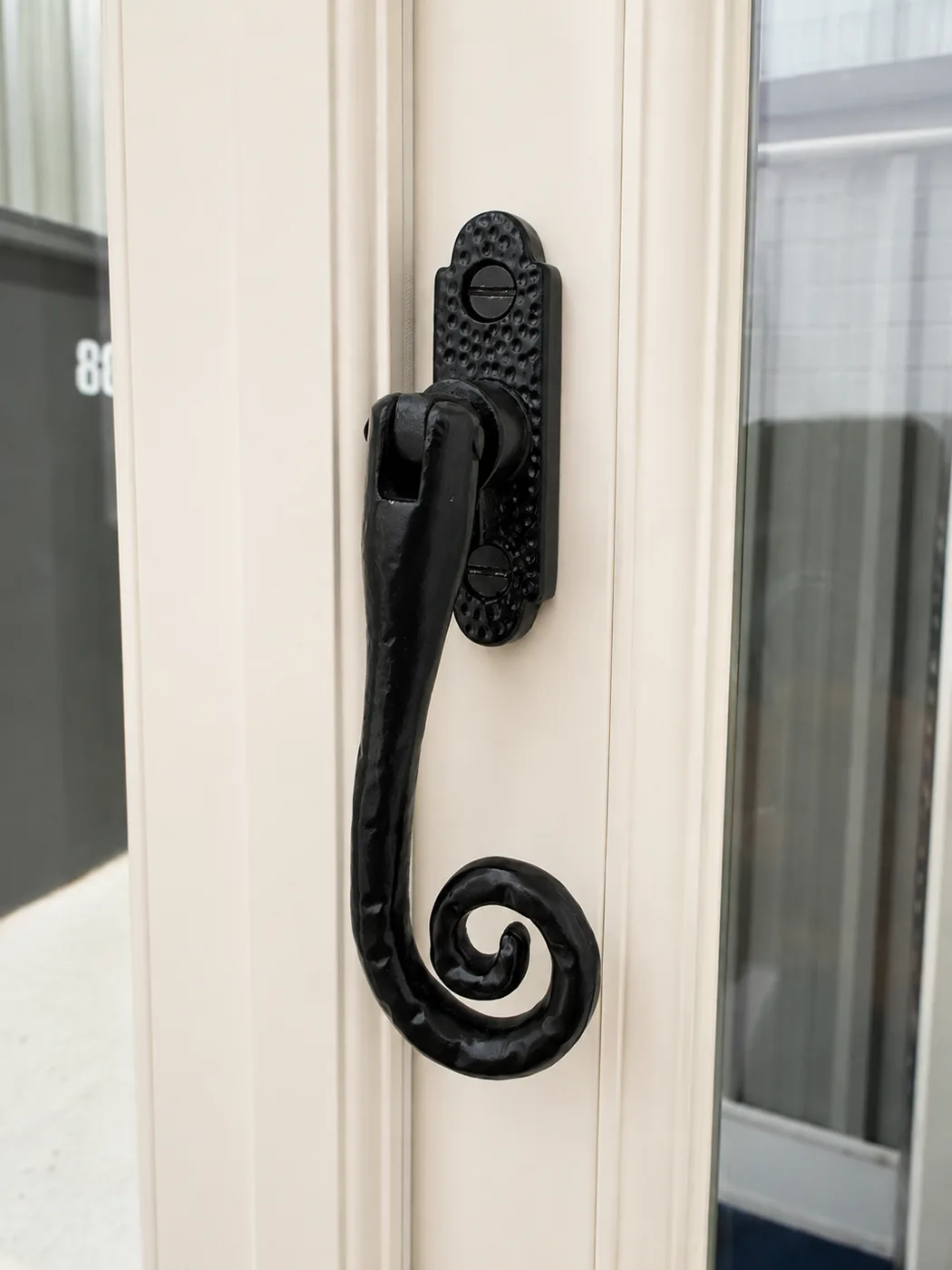 Black wrought iron monkey tail casement fastener on a painted timber window
