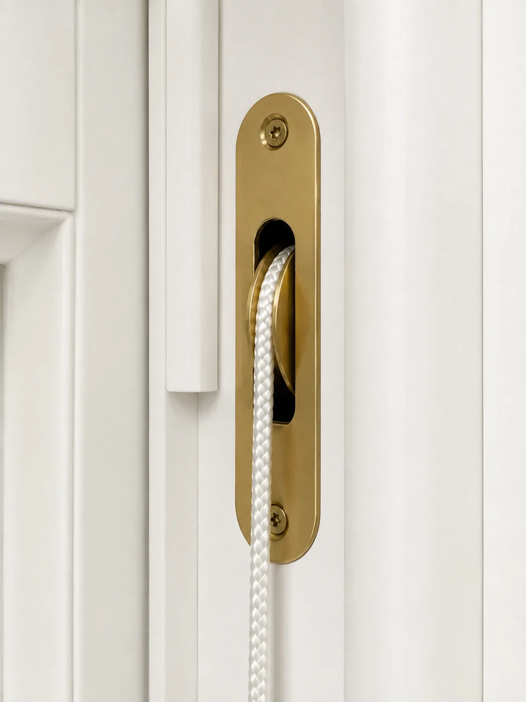 Polished brass sash pulley with cord, recessed into a white timber sash window