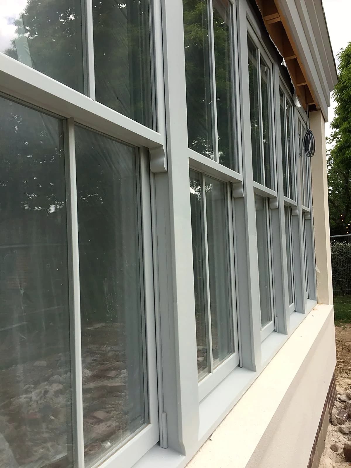 Angled detail of light grey timber sash windows with stone cills on the new-build bay