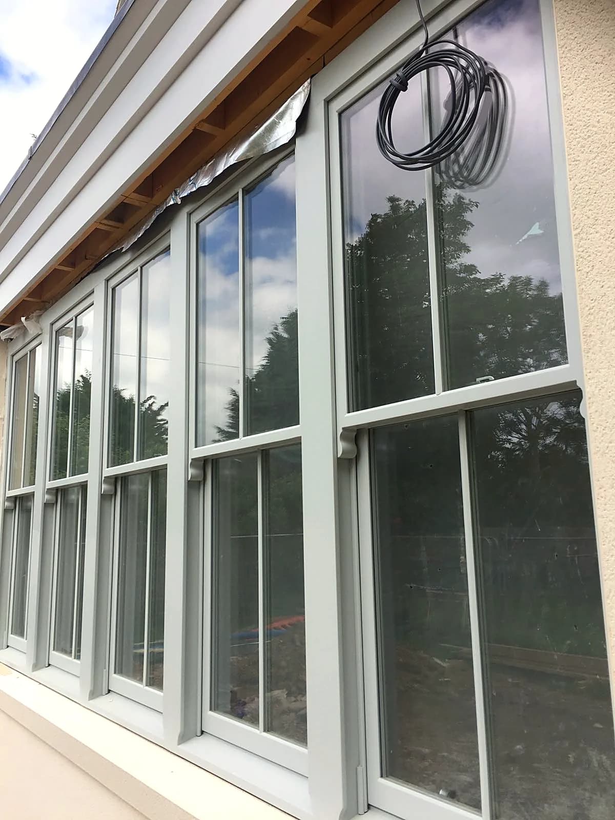 A run of tall light grey timber sash windows in the new-build garden room