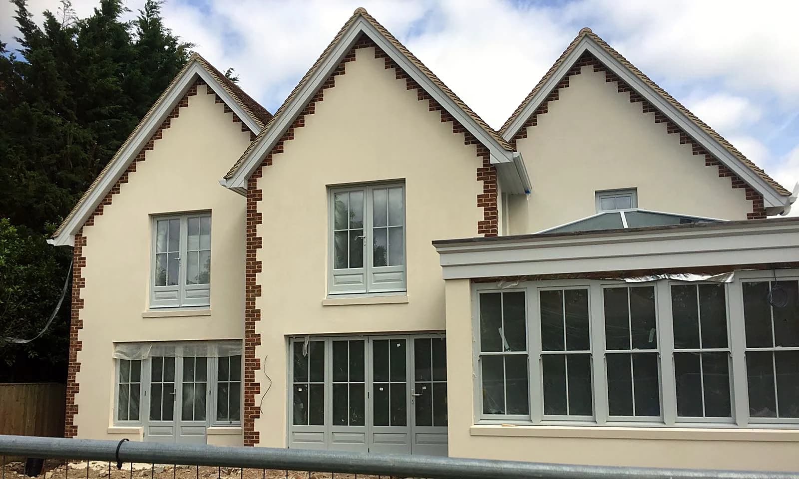 Front elevation of the new-build home during construction, with light grey timber sash windows and French doors installed