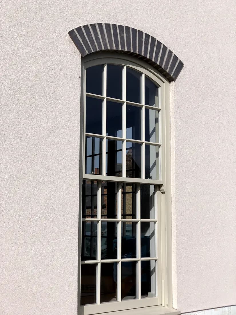 Tall arched-head timber sash window with fine glazing bars and a brick arch on a rendered house
