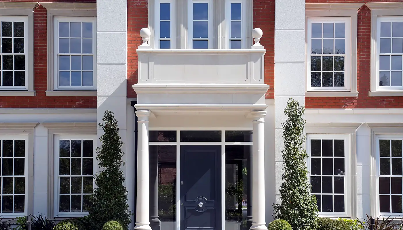 Columned entrance of a Surrey home flanked by timber Georgian sash windows in red brick