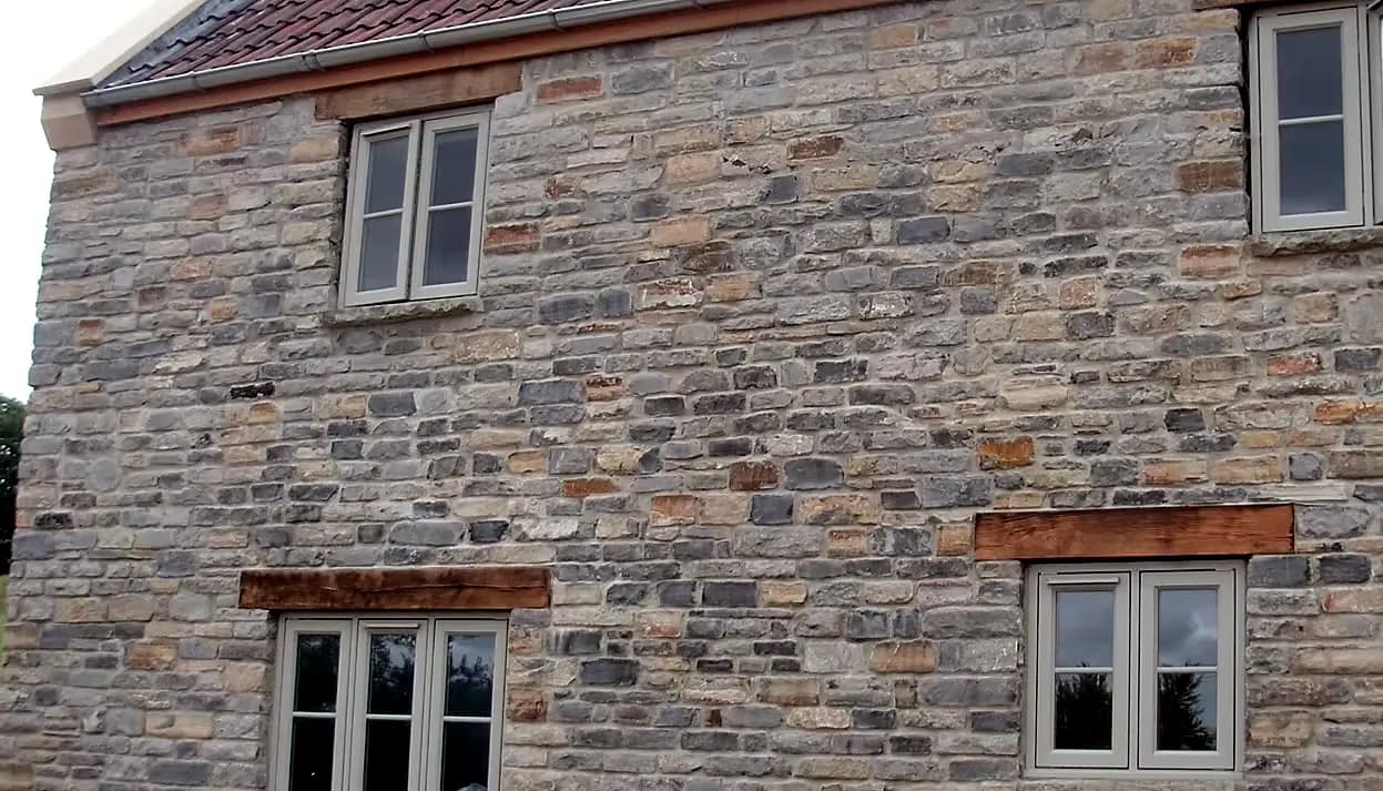 Sage-green timber casement windows under oak lintels in a natural stone house