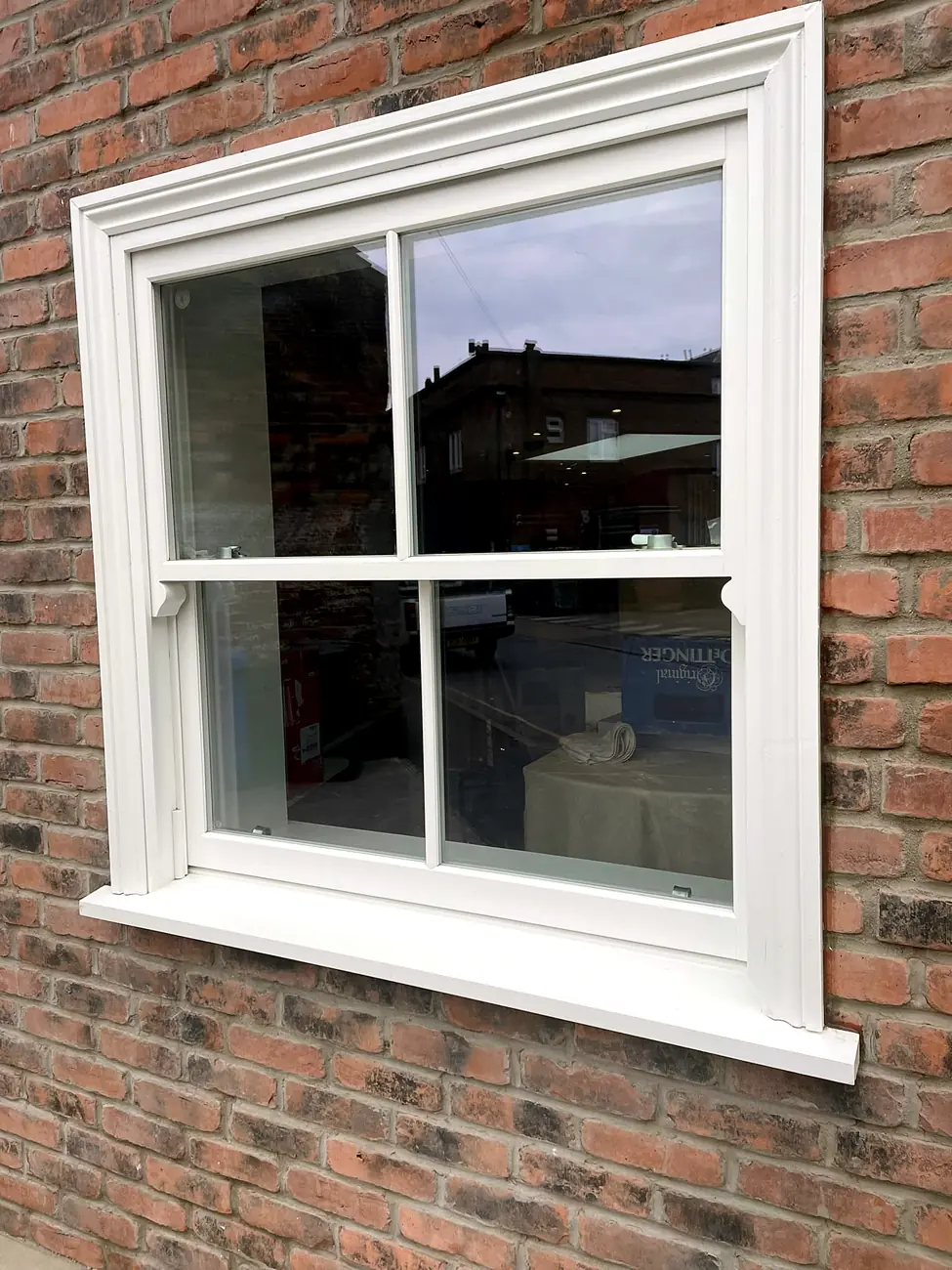 White timber Victorian two-over-two sash window with horns in a red-brick wall